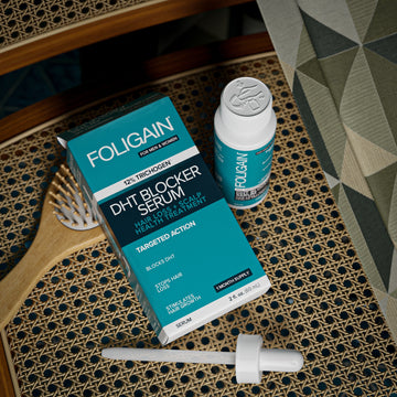 Overhead view of FOLIGAIN DHT serum box, bottle and dropper beside a hairbrush.