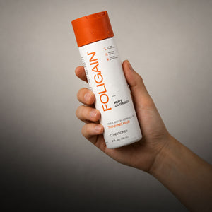 Hand holding FOLIGAIN men’s Triple Action Conditioner with 2% TRIOXIDIL.