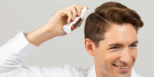 Man applying FOLIGAIN topical treatment to his scalp with a spray applicator.