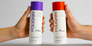 Hands holding FOLIGAIN women’s and men’s TRIOXIDIL conditioners with purple and orange caps.