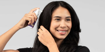 Woman applying FOLIGAIN topical treatment to her scalp with a spray applicator.