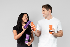 Woman and man holding purple and orange FOLIGAIN hair care bottles.