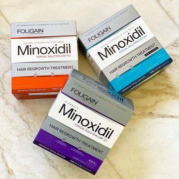 Three FOLIGAIN minoxidil formulas in orange, blue and purple boxes.