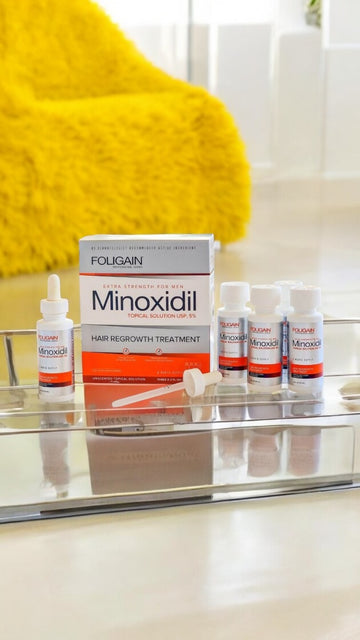 FOLIGAIN minoxidil box and bottles on a bathroom shelf beside a yellow towel.