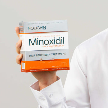 Hand holding a box of FOLIGAIN Men’s Minoxidil 5% Topical Solution.
