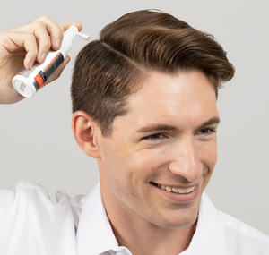 Man applying FOLIGAIN topical hair care along a part in his hair