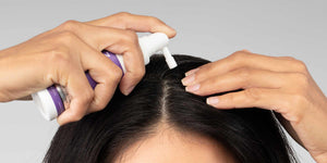 Woman parting her hair while applying FOLIGAIN topical treatment to her scalp