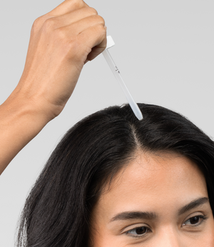 Dropper positioned along a woman’s parted hair to apply a topical scalp treatment