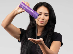 Woman dispensing FOLIGAIN liquid hair care from a purple bottle into her hand